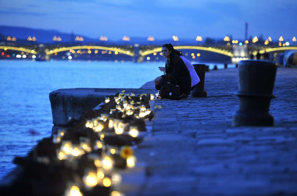 A woman crouches next to candles lit to commemorate victims among cast iron shoes, a memorial of Holocaust victims on the bank of River Danube, in Budapest, Hungary, Tuesday, April 16, 2013. (AP Photo/MTI, Noemi Bruzak)