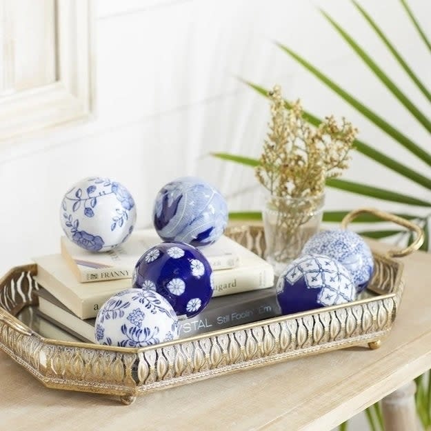 An elegant tray holds blue and white decorative balls on top of books, with a small vase of dried flowers