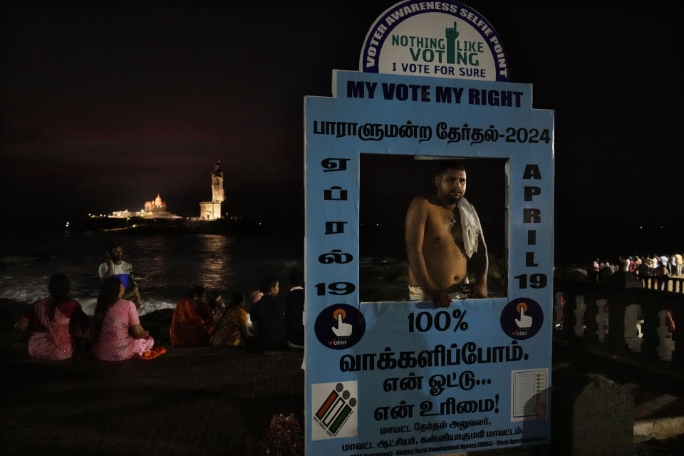 A man stands at an election photo prop with others wait to watch the sun rise at Kanyakumari, India, Monday, April 22, 2024. (AP Photo/Manish Swarup)