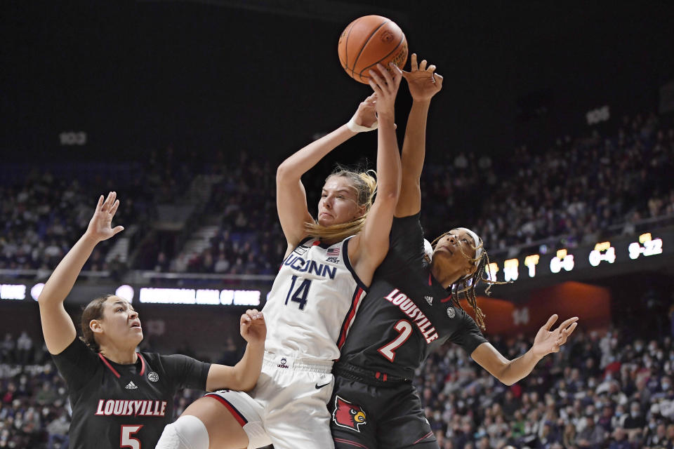 Connecticut's Dorka Juhasz (14) reaches up for a rebound against Louisville's Ahlana Smith (2) as Louisville's Mykasa Robinson (5) defends in the first half of an NCAA college basketball game, Sunday, Dec. 19, 2021, in Uncasville, Conn. (AP Photo/Jessica Hill)