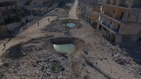 People stand near craters and damaged buildings in a rebel-held area of Aleppo, Syria. Handout via Reuters TV