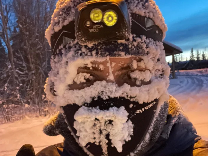 person wearing winter face gear and a headlamp covered in frost and snow in canada