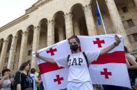 An opposition demonstrator holds a Georgian national flag at a rally in front of the Georgian Parliament building in Tbilisi, Georgia, Monday, June 24, 2019. Demonstrators have returned to parliament for daily rallies, demanding the release of detained protesters, the ouster of the nation's interior minister and changes in the electoral law to have legislators chosen fully proportionally rather than the current mix of party-list and single-mandate representatives. (AP Photo/Shakh Aivazov)