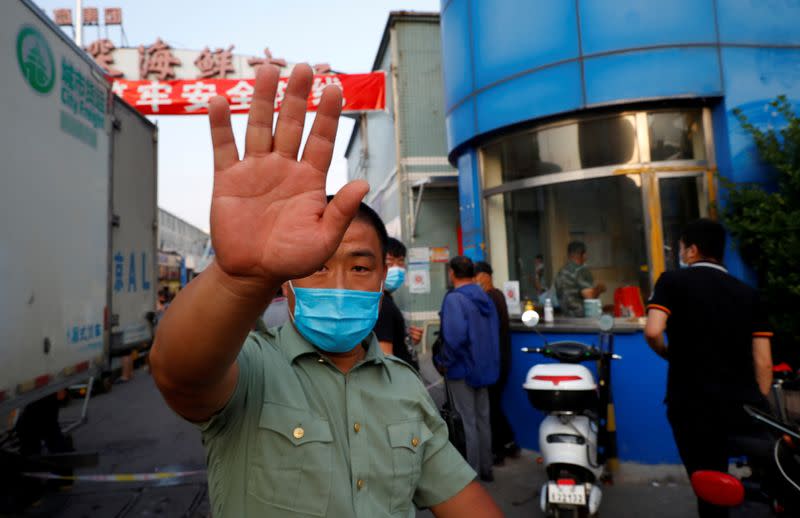 A security guard wearing a face mask tries to block the camera outside the Jingshen seafood market which has been closed for business after new coronavirus infections were detected, in Beijing