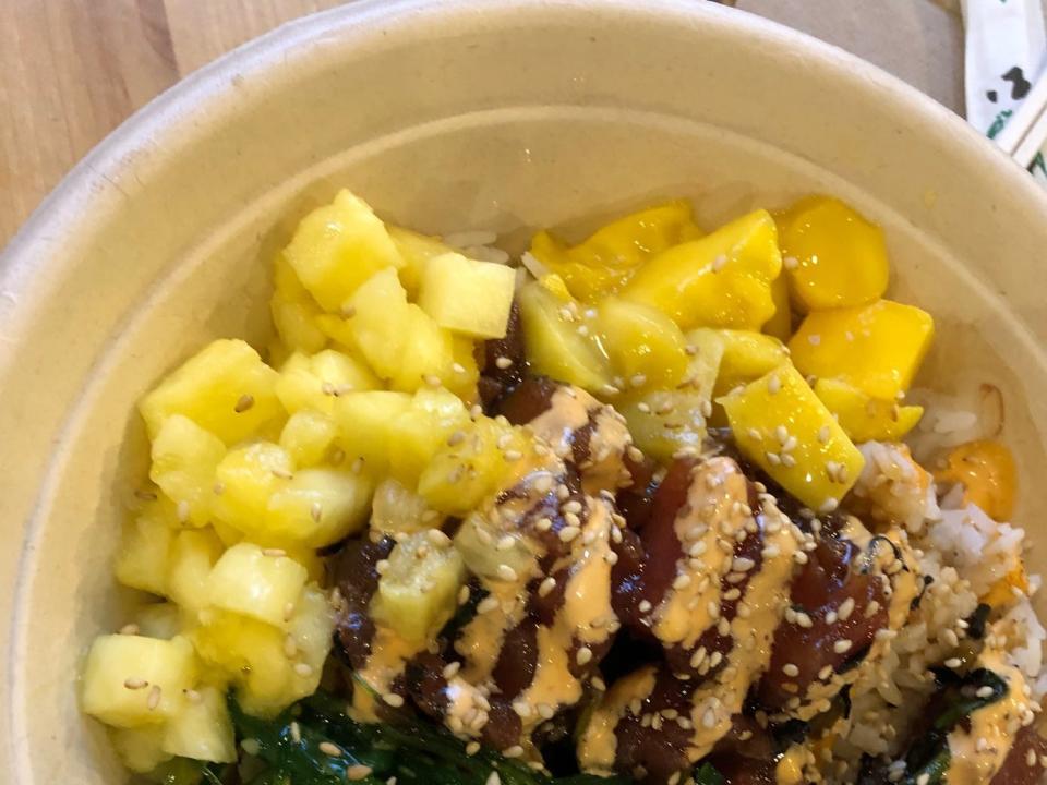 An Onolicious poke bowl from Poke Papa in Washington DC, topped with mango and pineapple, sitting on a wooden table