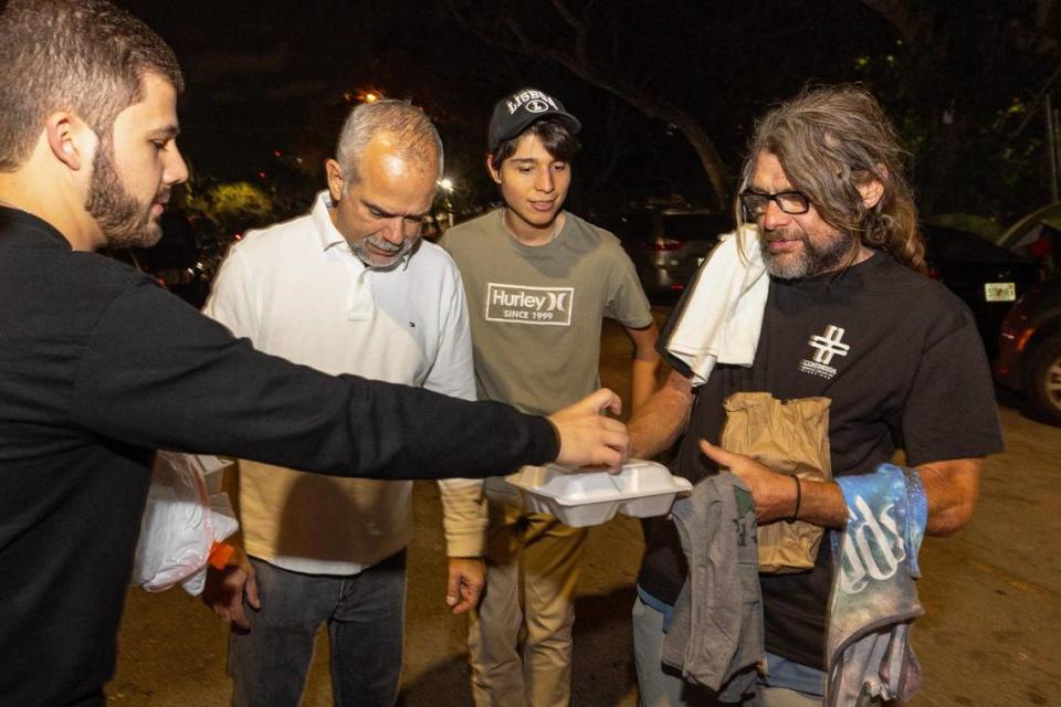 Hermanos de la Calle volunteer Andres Papa hands an unsheltered man a meal during a food distribution event on NW 17th Street in Miami, Florida, on Friday, December 22, 2023. D.A. Varela/dvarela@miamiherald.com