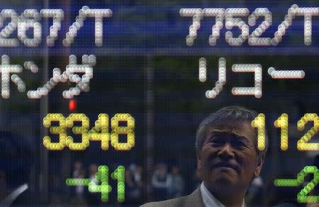 A man is reflected on an electronic stock quotation board outside a brokerage in Tokyo May 16, 2014. REUTERS/Yuya Shino