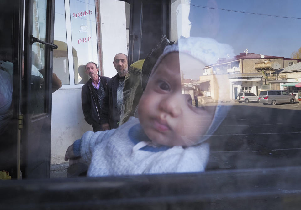 A street is reflected in a window as a baby sitting on his mother prepare to leave Stepanakert, the separatist region of Nagorno-Karabakh, Friday, Oct. 30, 2020. The Azerbaijani army has closed in on a key town in the separatist territory of Nagorno-Karabakh following more than a month of intense fighting. (AP Photo)