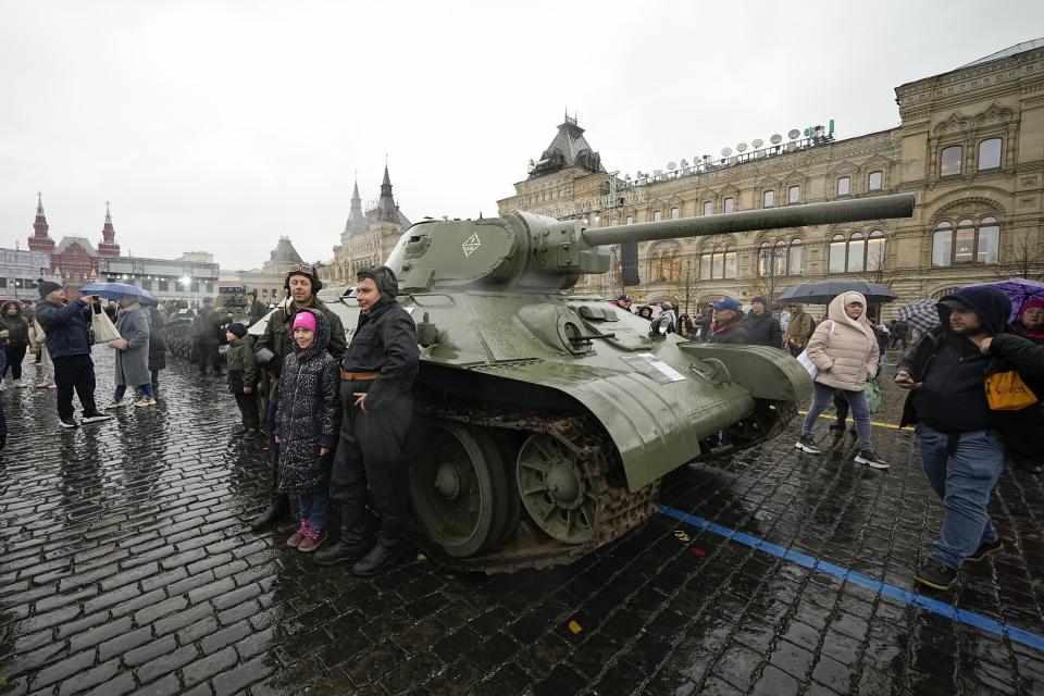 People pose for a photo in front of a Soviet era T-34 tank at an open air interactive museum to commemorate the 82nd anniversary of the World War II-era parade, at Red Square, in Moscow, Russia, on Monday, Nov. 6, 2023. The theatrical performance marks the 82nd anniversary of a World War II historic parade in Red Square and honored the participants in the Nov. 7, 1941 parade who headed directly to the front lines to defend Moscow from the Nazi forces. (AP Photo/Alexander Zemlianichenko)