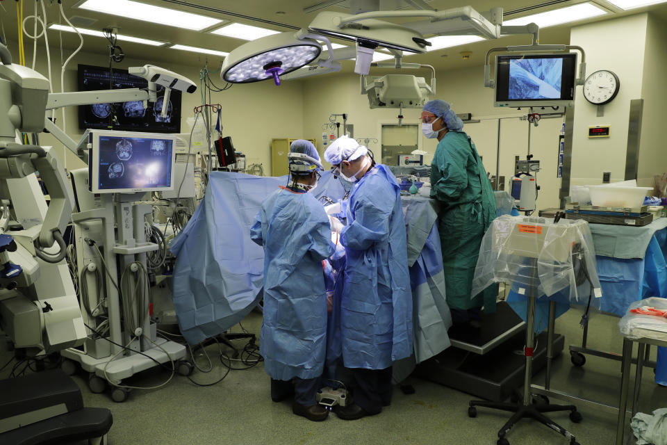 In this Jan. 14, 2020 photo, senior resident Dr. Ariana Barkley, left, assists neurosurgeon Dr. Andrew Ko, center, of the University of Washington School of Medicine, as surgical technician Melodie White, right, looks on as Genette Hofmann undergoes brain surgery at Harborview Medical Center in Seattle in hopes of reducing the epileptic seizures that had disrupted her life for decades. At the same time, Hofmann agreed to donate a small bit of her healthy brain tissue to researchers, who were eager to study brain cells while they were still alive, joining a long line of epilepsy patients who've helped scientists reveal basic secrets of the brain. (AP Photo/Ted S. Warren)