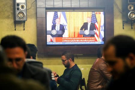 Palestinians play cards as a TV screen shows a joint press conference by U.S. President Donald Trump and Israeli Prime Minister Benjamin Netanyahu, in a coffee shop in the West Bank city of Hebron February 15, 2017. REUTERS/Mussa Qawasma