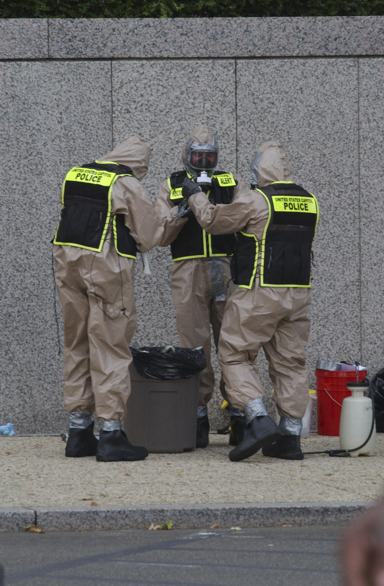 Three people in hazmat suits prepare to enter a building.