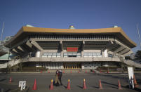 A man and a woman walk past the Nippon Budokan arena, one of the venues planned to be used in the rescheduled Tokyo Olympics, in Tokyo on Thursday, Jan. 21, 2021. The postponed Tokyo Olympics are to open in just six months. Local organizers and the International Olympic Committee say they will go ahead on July 23. But it’s still unclear how this will happen with virus cases surging in Tokyo and elsewhere around the globe. (AP Photo/Hiro Komae)