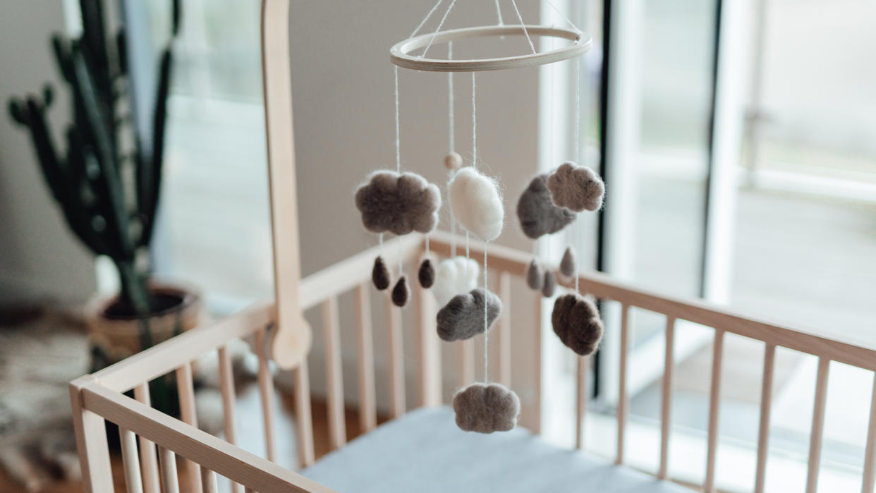  Photo of a baby mobile with soft cloud shapes and rain drops hanging above an empty crib. 