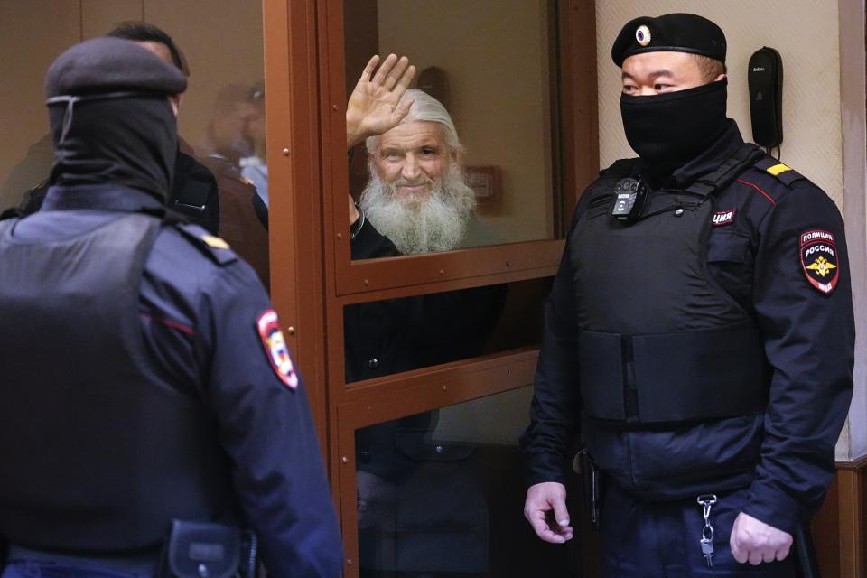 Nikolai Romanov, a former monk known as Father Sergiy until he was excommunicated by the Russian Orthodox Church, waves standing behind a glass cage during his trial in Moscow, Russia, Friday, Jan. 27, 2023. The monk, who denied that the coronavirus existed and challenged the Kremlin, was handed a new prison sentence Friday on charges of inciting hatred. (AP Photo/Alexander Zemlianichenko)