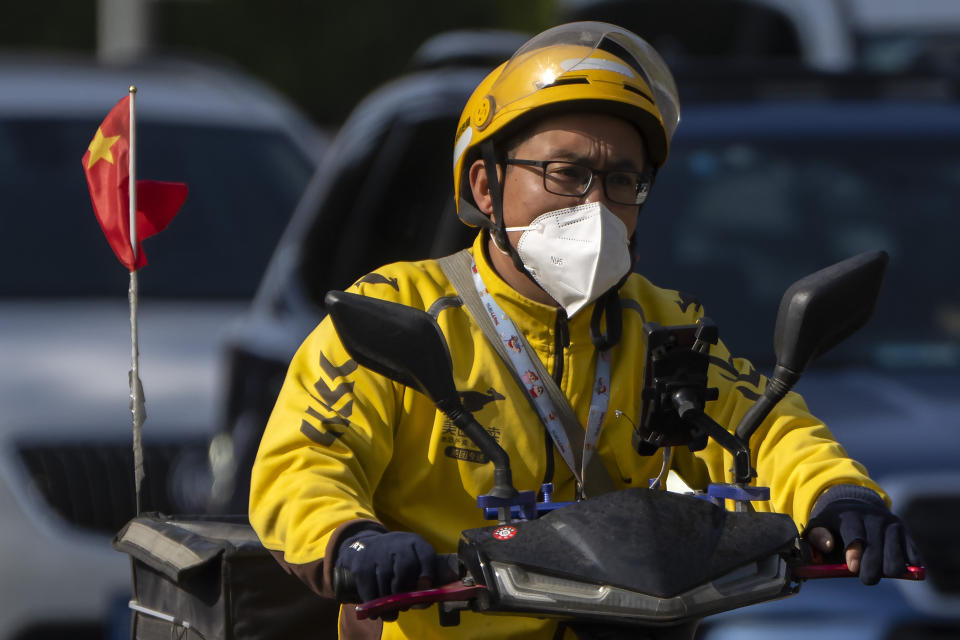 A delivery driver wearing a face mask rides a scooter with a Chinese flag along a street in Beijing, Tuesday, Nov. 1, 2022. Shanghai Disneyland was closed and visitors temporarily kept in the park for virus testing, the city government announced, while social media posts said some amusements kept operating for guests who were blocked from leaving. (AP Photo/Mark Schiefelbein)