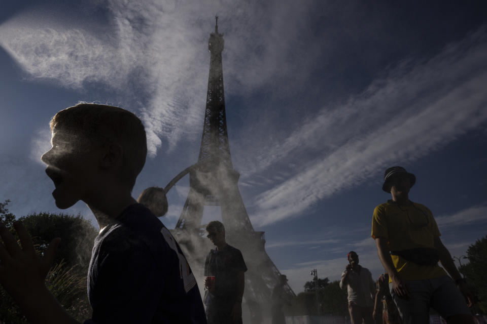 People cool off under a mist outside the Eiffel Tower Stadium at the 2024 Summer Olympics, Sunday, July 28, 2024, in Paris, France. (AP Photo/Louise Delmotte)