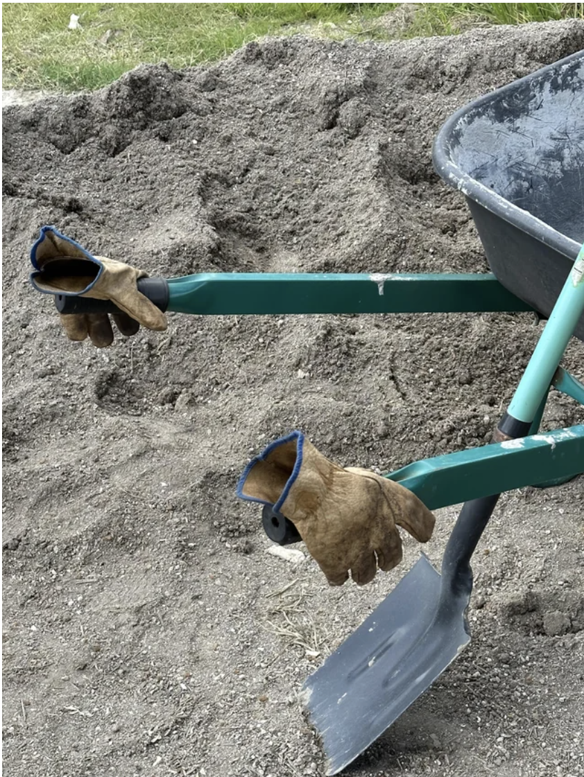 Work gloves attached to a wheelbarrow in dirt