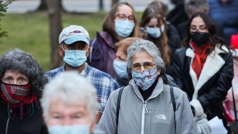 PHOTO: A crowd of people wearing masks walk down an alley from Main Street, Dec. 21, 2021, in Patchogue, N.Y. (Newsday Llc/Newsday via Getty Images)