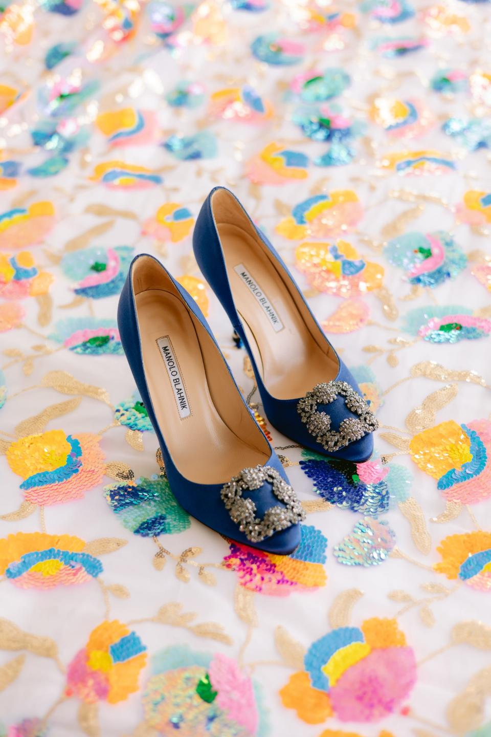 A pair of blue Manolo Blahniks sit on a rainbow, floral backdrop.