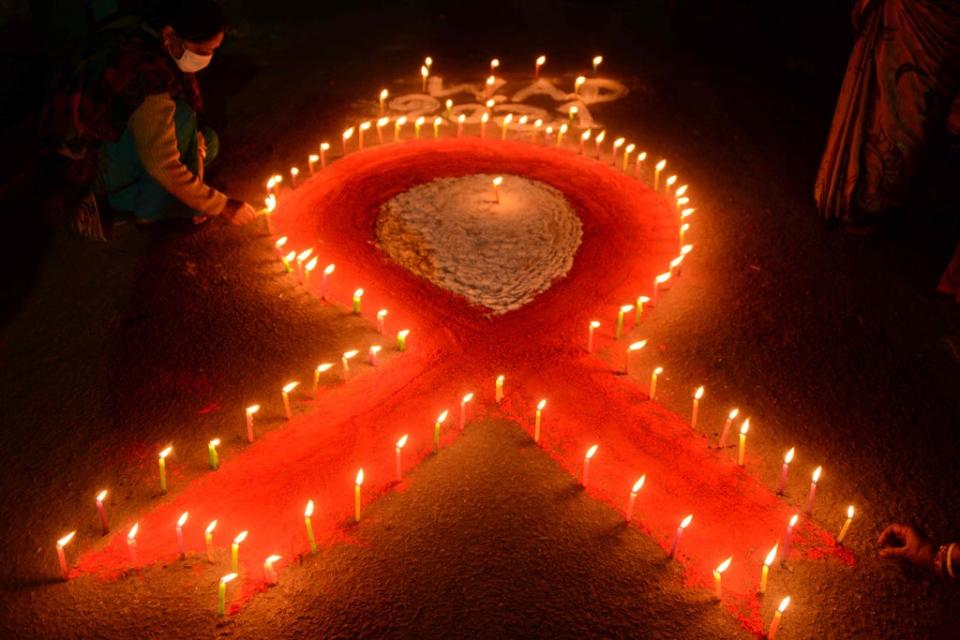 A volunteer lights candles forming the shape of a red ribbon during an awareness event organised on the eve of World AIDS Day (AFP via Getty Images)