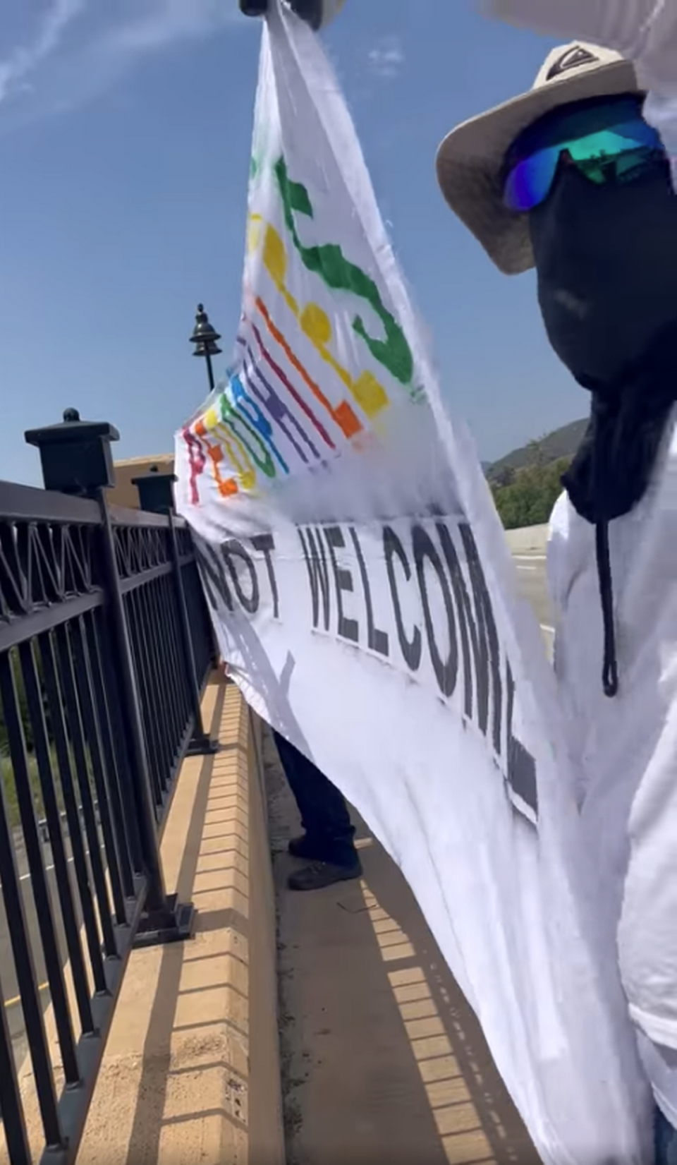 Two masked men hold up a banner reading “Pedophiles not welcome,” with “pedophiles” in rainbow colors, on June 10, 2023, on the Los Osos Valley Road overpass in San Luis Obispo.