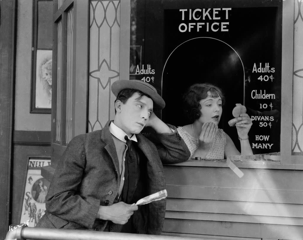 1924: American comedian Buster Keaton (1895-1966) standing outside the box office clutching his dollar bill while Ruth Holly applies her make-up in the film 'Sherlock Junior'.