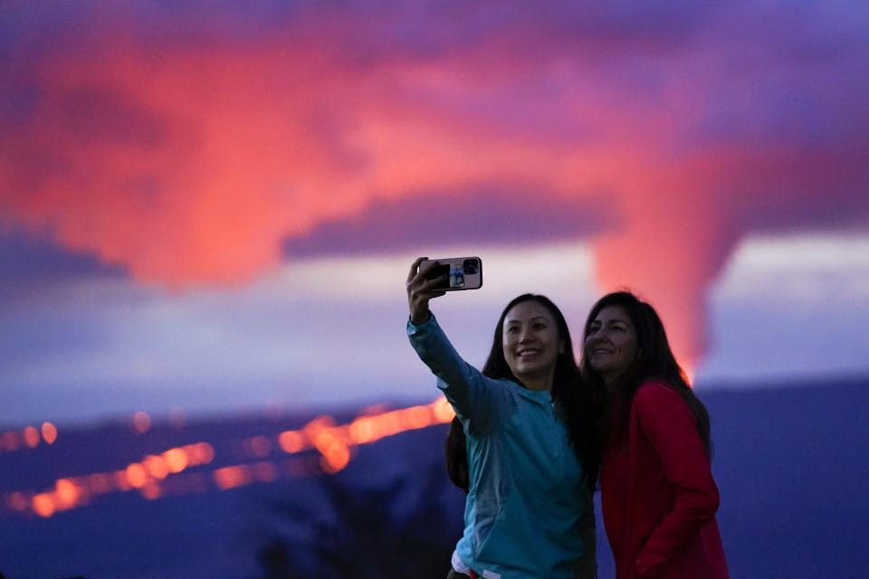 Ingrid Yang, left, and Kelly Bruno, both of San Diego, take a photo in front of lava erupting from Hawaii's Mauna Loa volcano Wednesday, Nov. 30, 2022, near Hilo, Hawaii. (AP Photo/Gregory Bull)