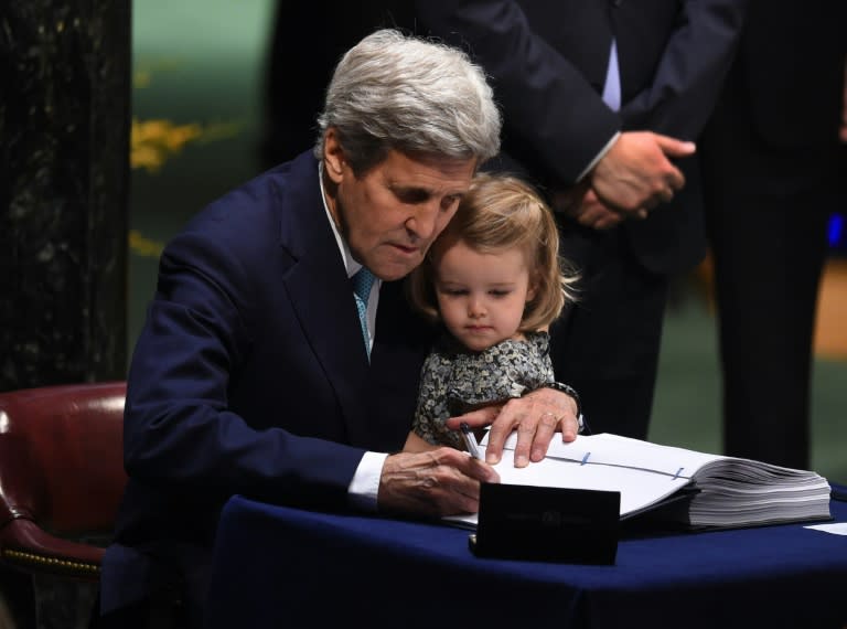 US Secretary of State John Kerry signs the book holding his granddaughter, Isabelle Dobbs-Higginson, during the signature ceremony for the Paris Agreement at the United Nations General Assembly Hall on April 22, 2016 in New York