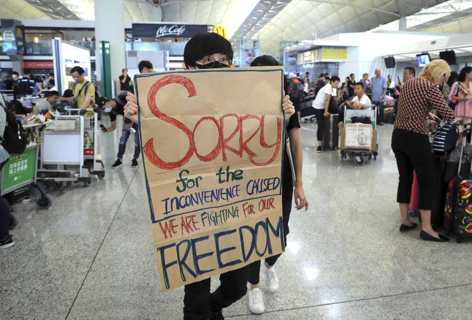 A protester shows a placard to stranded travelers during a demonstration at the Airport in Hong Kong, Tuesday, Aug. 13, 2019. Protesters severely crippled operations at Hong Kong's international airport for a second day Tuesday, forcing authorities to cancel all remaining flights out of the city after demonstrators took over the terminals as part of their push for democratic reforms. (AP Photo/Kin Cheung)