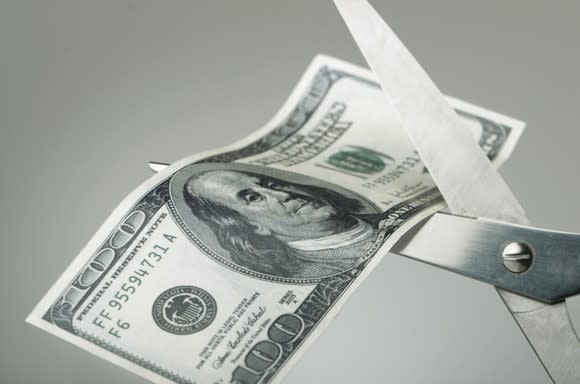 Pair of scissors cutting a $100 bill