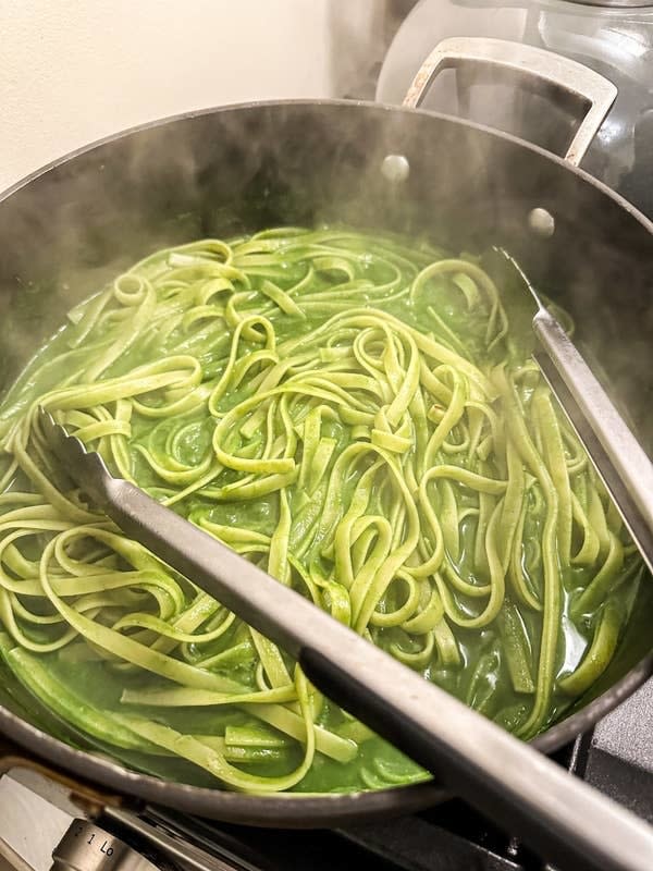 Pasta being cooked in a pot with tongs