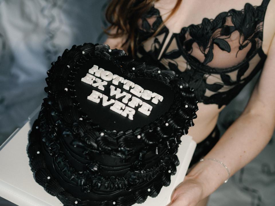 A woman in black lingerie holding a cake saying "Hottest Ex-Wife Ever."