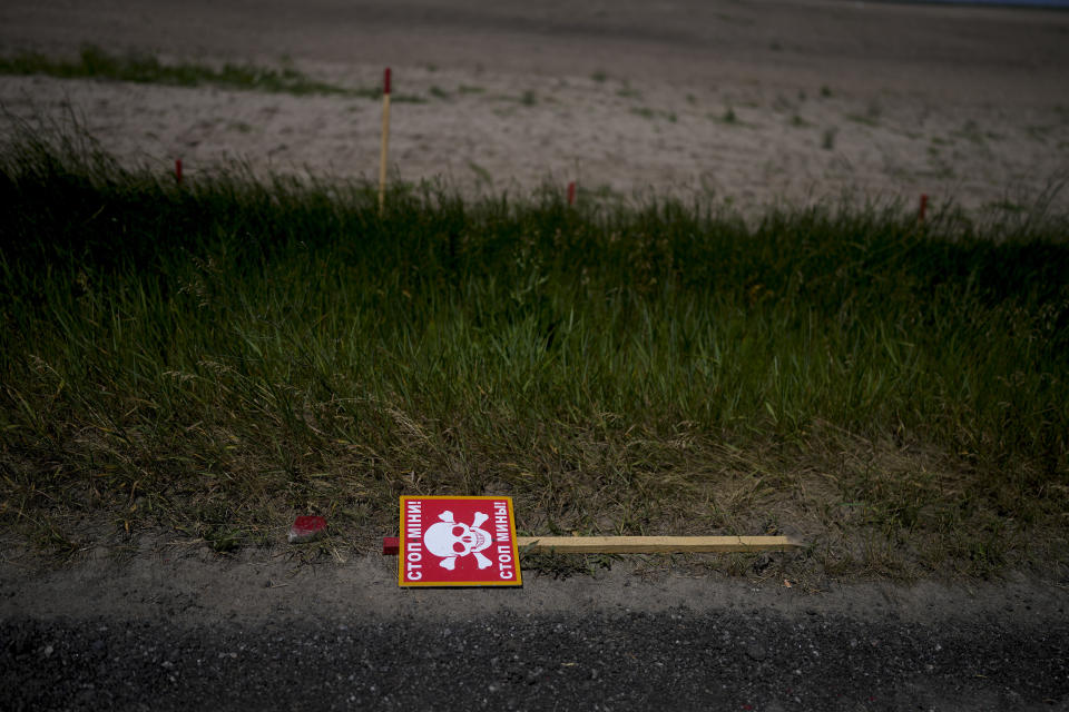 A poster warning about mines lies beside a road in Lypivka, on the outskirts of Kyiv, Ukraine, Tuesday, June 14, 2022. Russia’s invasion of Ukraine is spreading a deadly litter of mines, bombs and other explosive devices that will endanger civilian lives and limbs long after the fighting stops. (AP Photo/Natacha Pisarenko)