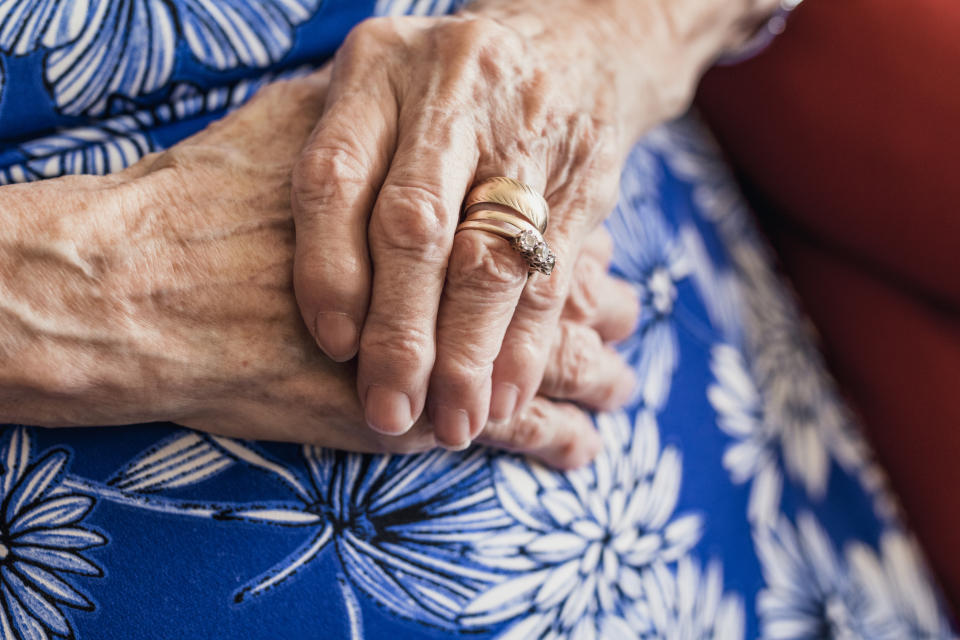 Elderly person's hands with wedding rings resting on a floral patterned garment