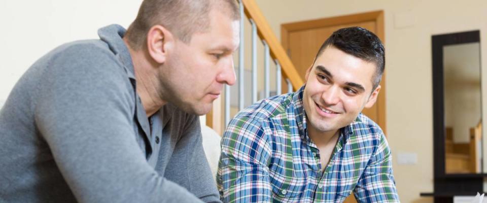 Adult smiling man helping friend to fill banking document indoor