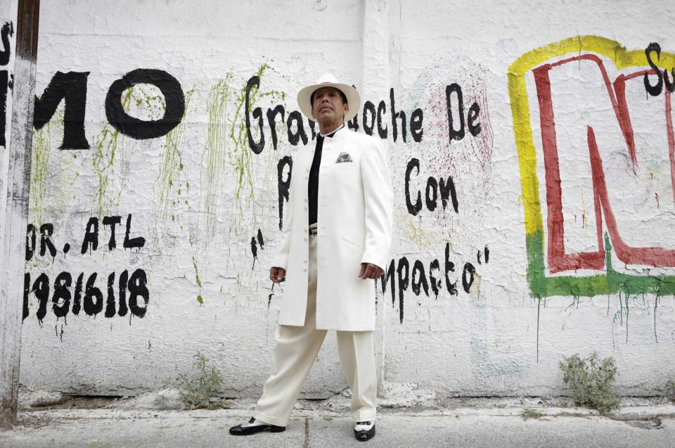 Macias Sotelo wears his "Pachuco" outfit while posing for a photograph next to a wall with graffiti in Mexico City