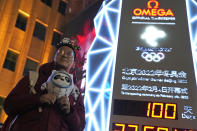 A supporter of the 2022 Beijing Winter Olympics poses for photos with a countdown clock as it crosses into the 100 days countdown to the opening of the Winter Olympics in Beijing, China, Tuesday, Oct. 26, 2021. (AP Photo/Ng Han Guan) ///