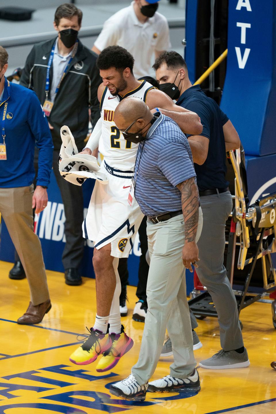 Nuggets guard Jamal Murray is helped off the court by a trainer.