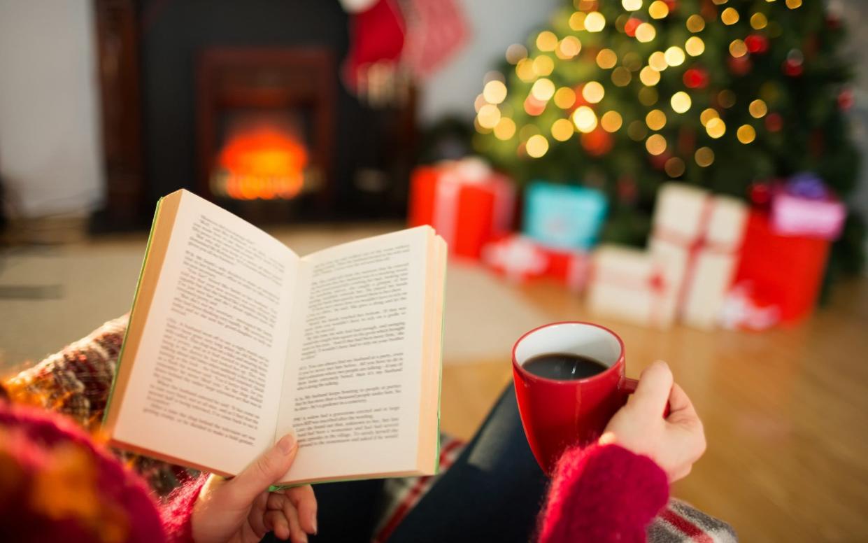 Woman reading a book and drinking coffee at christmas at home in the living room - Wavebreakmedia/iStockphoto