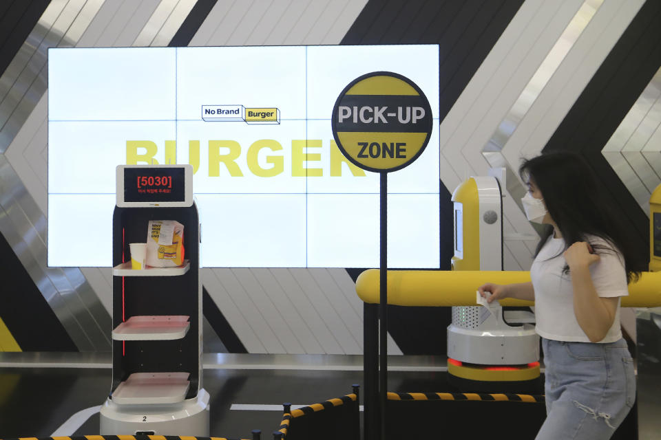 In this Sunday, Sept. 13, 2020, photo, a customer moves to pick up her takeout bag with food from a robot at No Brand Burger in Seoul, South Korea. These robotic services, with not a single face-to-face interaction, have been seen as a selling point amid the coronavirus pandemic and its restrictions. (AP Photo/Ahn Young-joon)