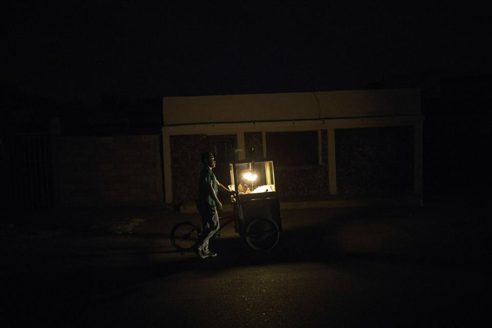 In this May 15, 2019 photo, popcorn vendor Raul Navas looks for customers during a black out in Maracaibo, Venezuela. Navas uses a kerosene lamp to illuminate his cart as he walks the streets during the blackout. (AP Photo/Rodrigo Abd)