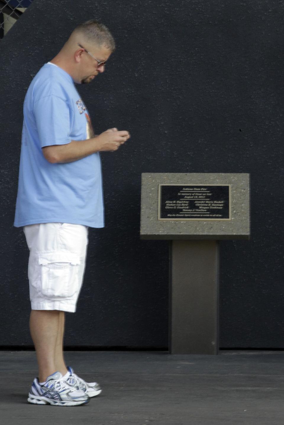 A visitor to the Indiana State Fair on opening day sends a text on his phone beside the memorial to the seven killed in the Aug. 13, 2011 stage collapse during a Sugarland concert at the fair in Indianapolis, Aug. 3, 2012. The memorial was virtually unnoticed by fair visitors. (AP Photo/Michael Conroy)