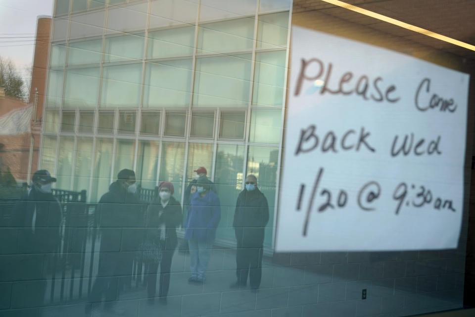 FILE - In this Jan. 19, 2021 file photo, people waiting in line are reflected in the glass windows of a vaccination site in Paterson, N.J. A sign on the door of the vaccination site, which takes walk-ins rather than appointments, said it would be open the following day. Having trouble booking a COVID-19 vaccine appointment online? Some people have turned to social media vaccine “bots” that scan the patchwork of vaccination websites and send alerts when a clinic is ready to book new patients. (AP Photo/Seth Wenig, File)