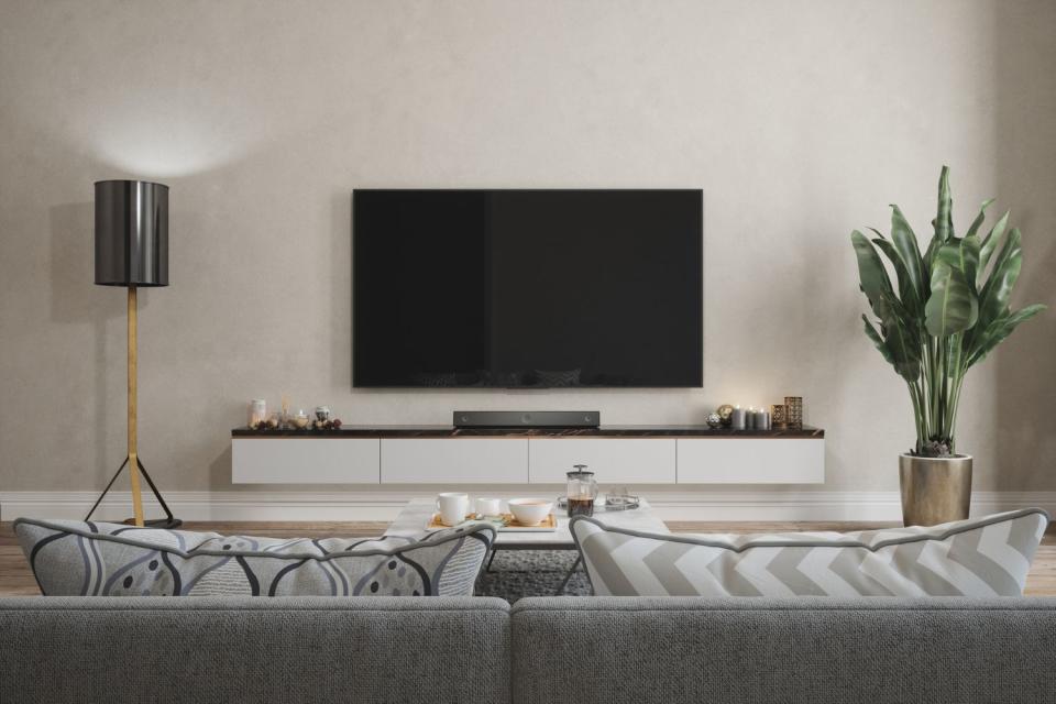 A flat-screen TV sits stop a TV stand against a white wall with a couch in the foreground.