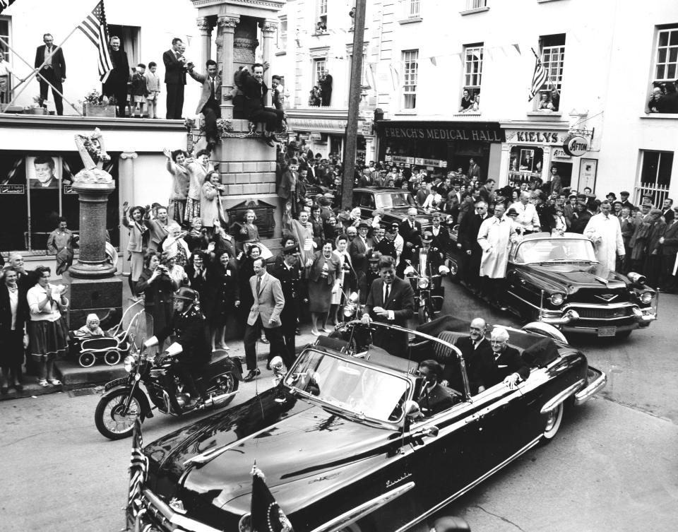 Cheering people cram the streets and even perch on the narrow cornice of a building as they welcome U.S. President John F. Kennedy on his visit at their hometown New Ross, Ireland, June 27, 1963.