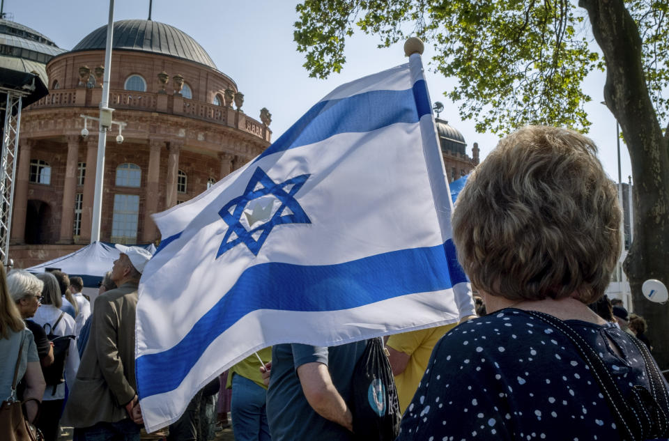 A woman holds an Israeli flag as she takes part in a demonstration against a concert later the day of former Pink Floyd musician Roger Waters in the Festhalle, background, in Frankfurt, Germany, Sunday, May 28, 2023. The Festhalle was the place where in the night of broken glasses 1938 about 3000 Jewish men where gathered to deport them to concentration camps. (AP Photo/Michael Probst)