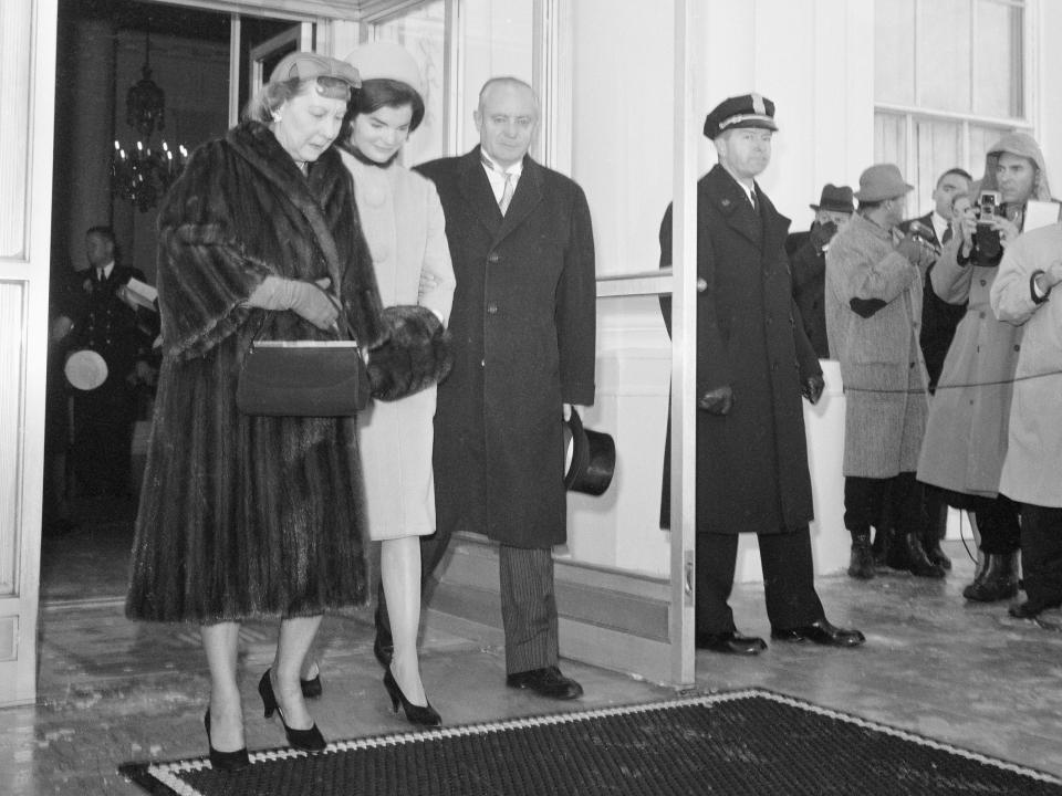 Eisenhower in a long fur coat, hat, gloves, purse and heels walking with Kennedy.