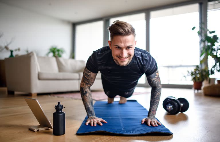 Front view portrait of man with tablet doing workout exercise indoors at home.