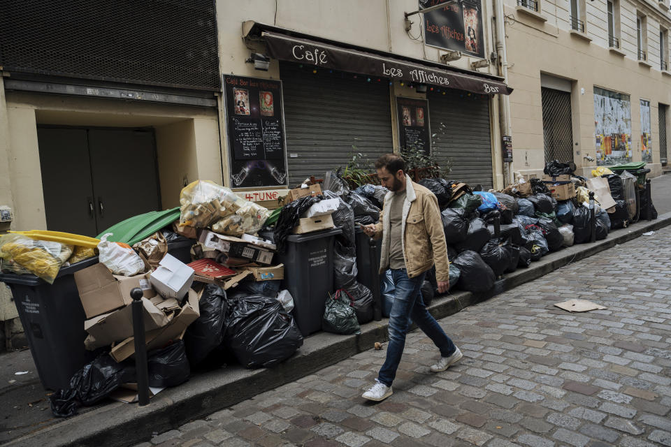 A man walks past uncollected garbage in Paris, Monday, March 13, 2023. A contentious bill that would raise the retirement age in France from 62 to 64 got a push forward with the Senate's adoption of the measure amid strikes, protests and uncollected garbage piling higher by the day. (AP Photo/Lewis Joly)